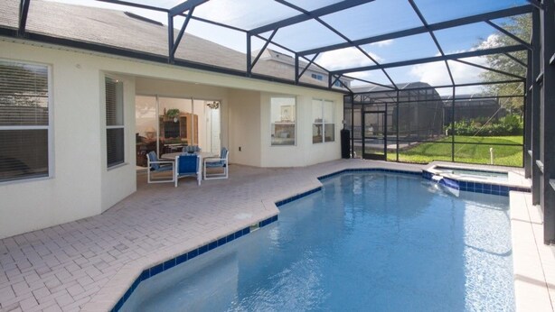 Ein Schwimmbad mit Glasveranda, eine Terrasse mit Sitzgelegenheiten und Blick auf den Garten.