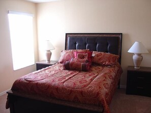 A neatly made bed with a patterned bedspread, two bedside lamps, and a window with blinds.