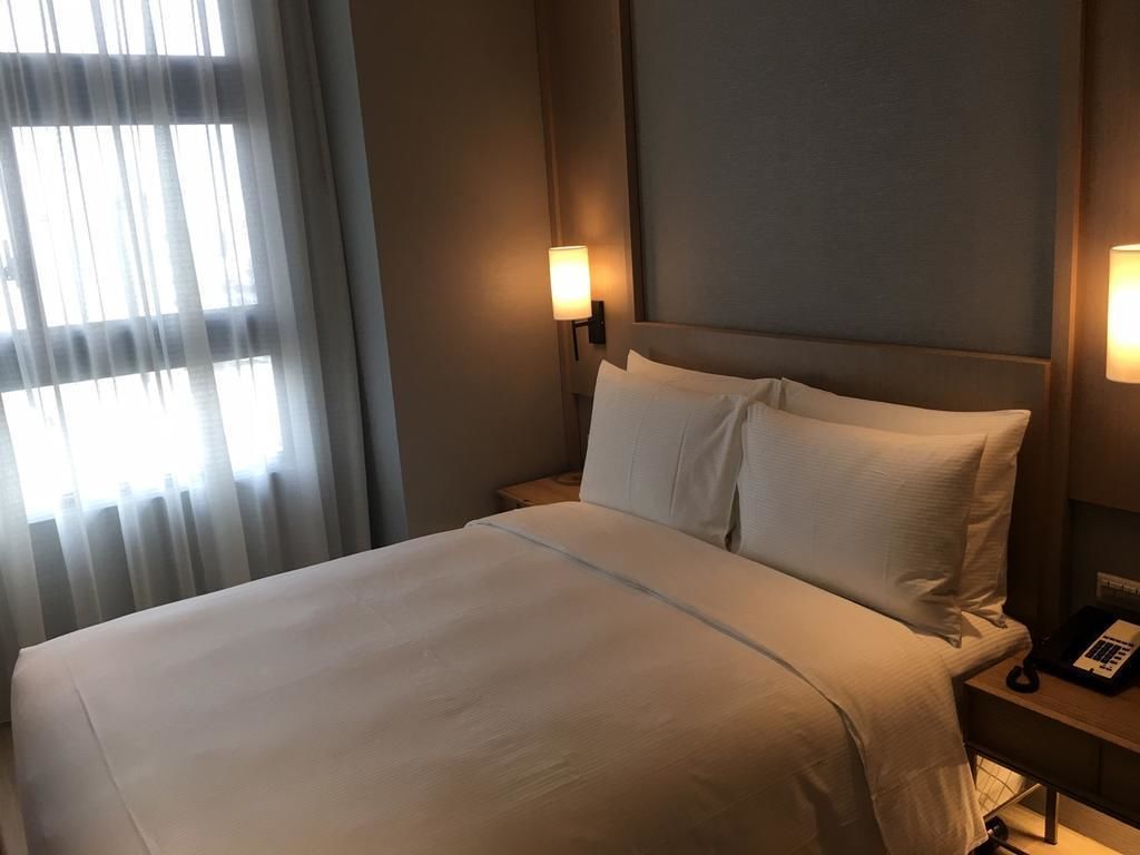 A neatly made bed with white linens, two bedside lamps, and a nightstand with a telephone.