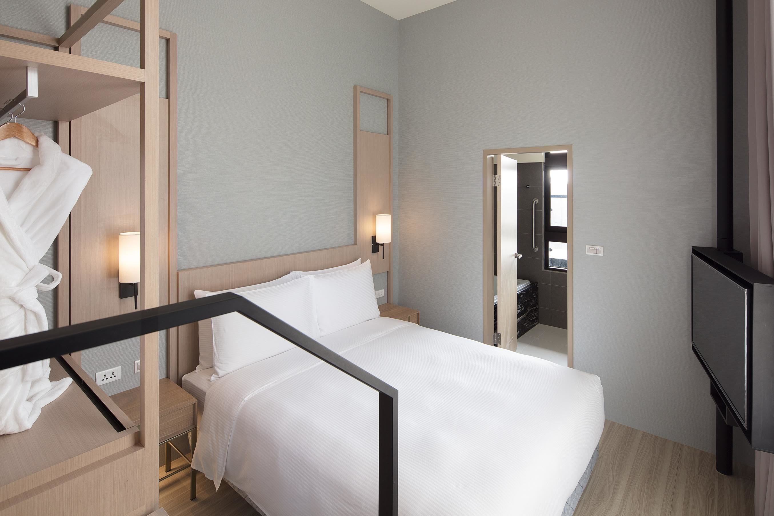 Una habitación de hotel con cama, mesitas de noche, televisión, espejo y armario.
