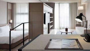 A hotel room with a bed, a desk with a magazine, a lamp, a sofa, and a TV.