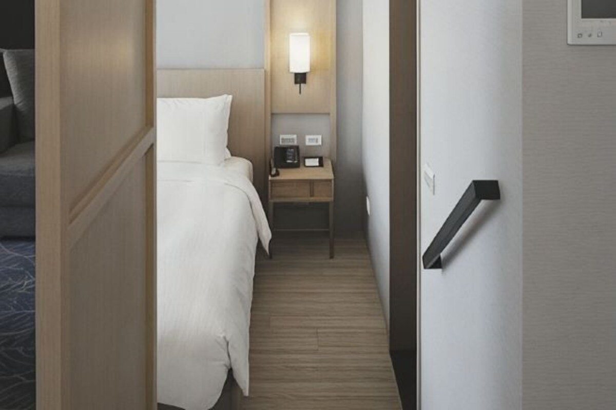 A hotel room with a bed, bedside table, lamp, and a door.