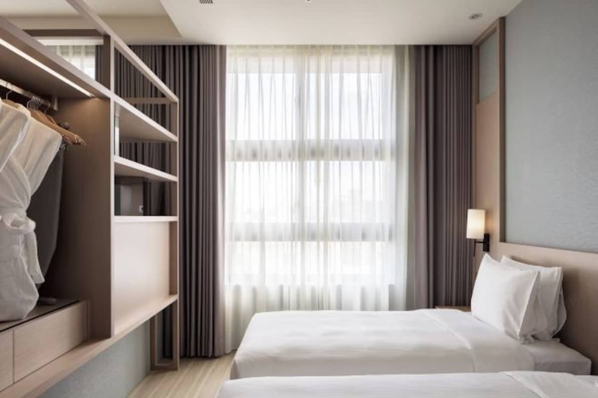 A hotel room with a bed, a wardrobe, and a large window with curtains.