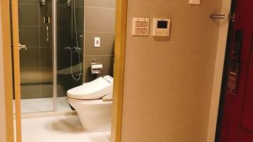 Un baño moderno con ducha envuelta en vidrio, inodoro y panel de control en la pared.