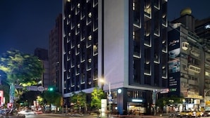 A modern hotel with a prominent vertical design, multiple balconies, and a well-lit facade. - Jolley Hotel (Taipei)