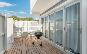 Un balcon doté d’une terrasse en bois, d’un barbecue et d’une clôture blanche.