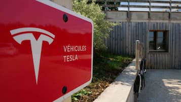 Un letrero rojo con el logo de Tesla y la inscripción 'VÉHICULES TESLA', que indica una estación de carga para vehículos Tesla.