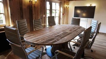 A conference room with a large wooden table, six chairs, and a TV screen displaying the time.