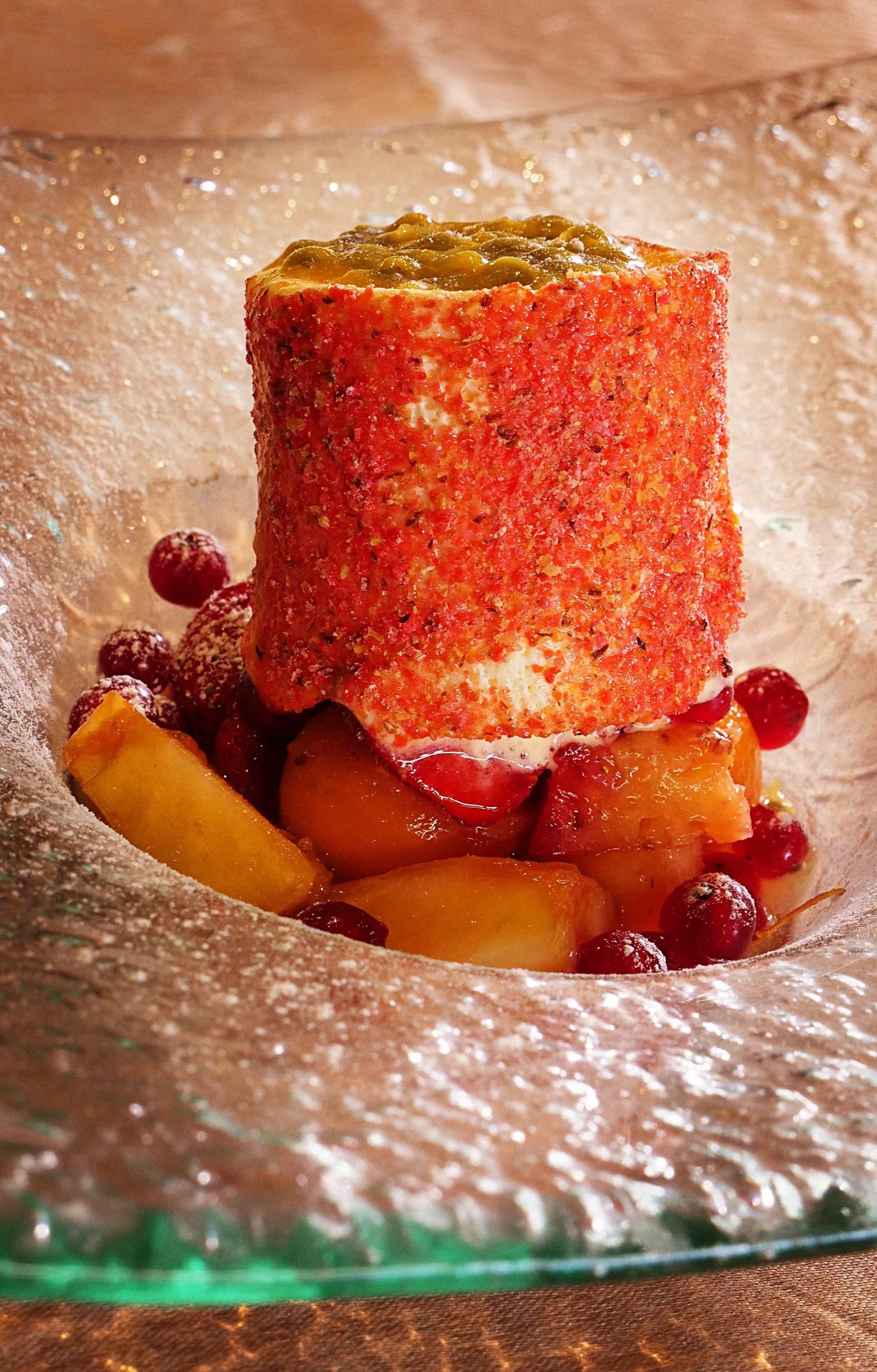 En dessert med en rustik, rødbrun overflade, måske crumble eller crumblekage, serveret på et glasfad med et drys flormelis og omgivet af frugtstykker.
