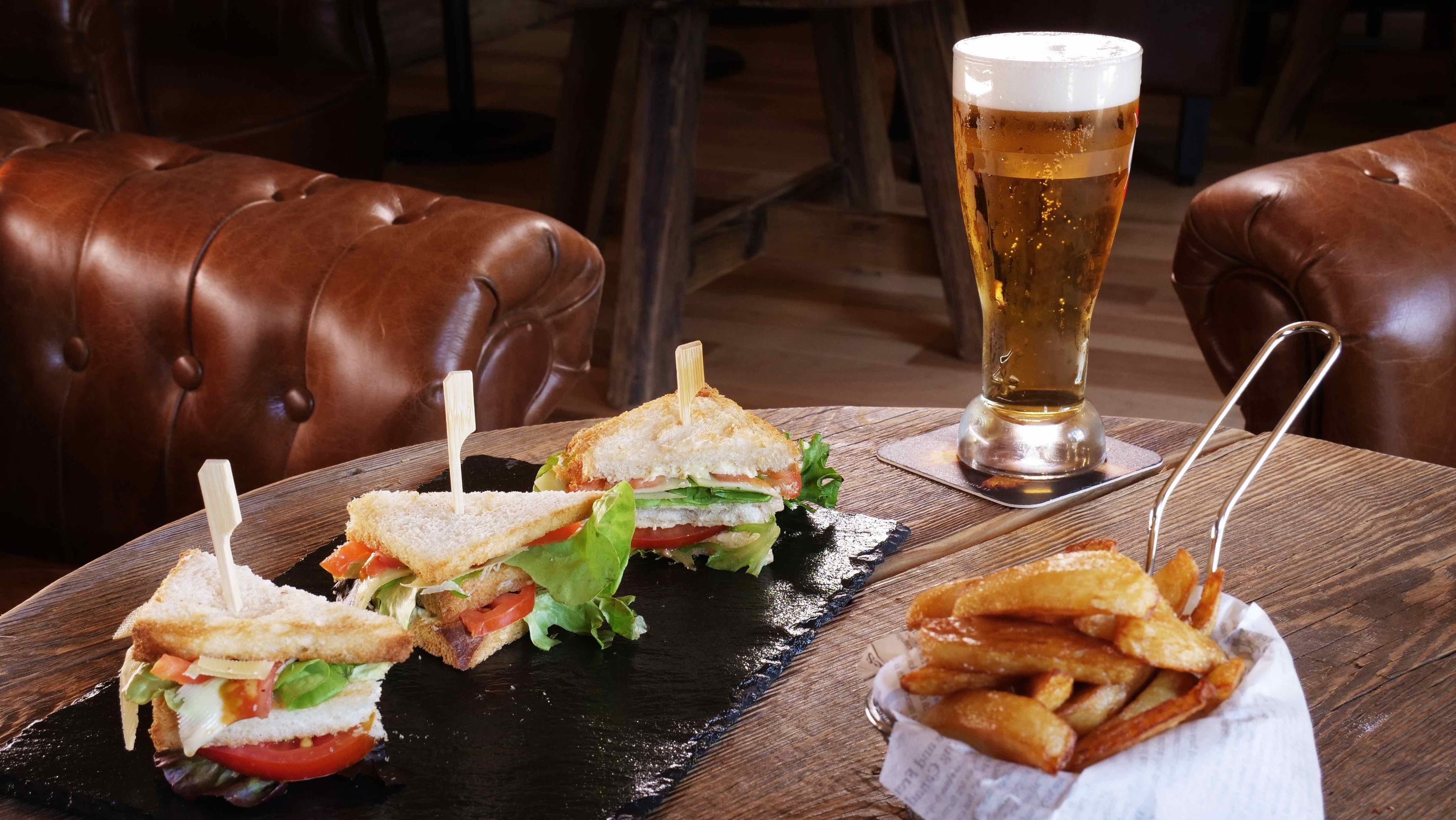 Una mesa con dos sándwiches, una jarra de cerveza y una cesta de papas fritas.