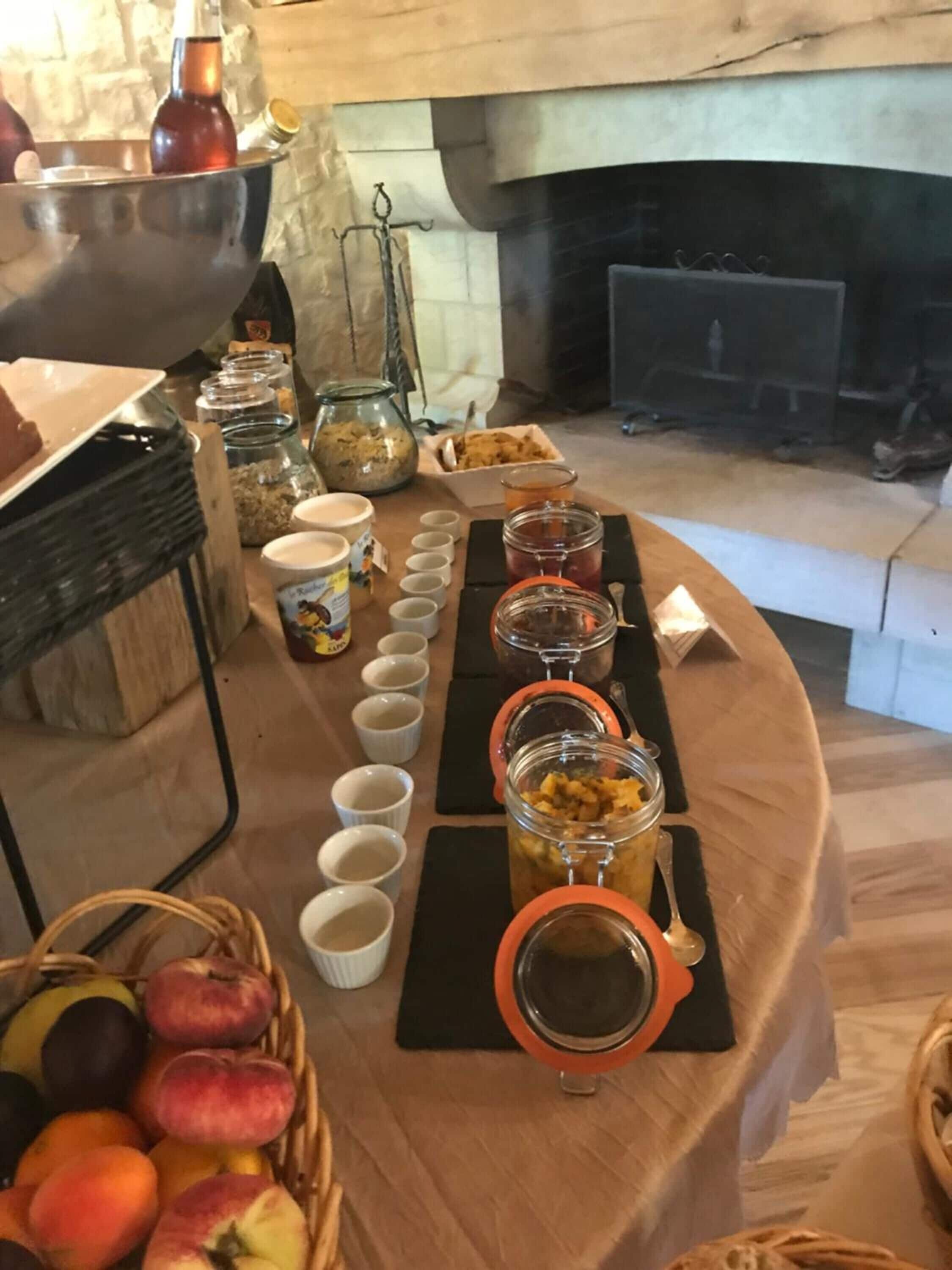 A buffet table with various food items and beverages, a fireplace in the background, and a basket of fruits.