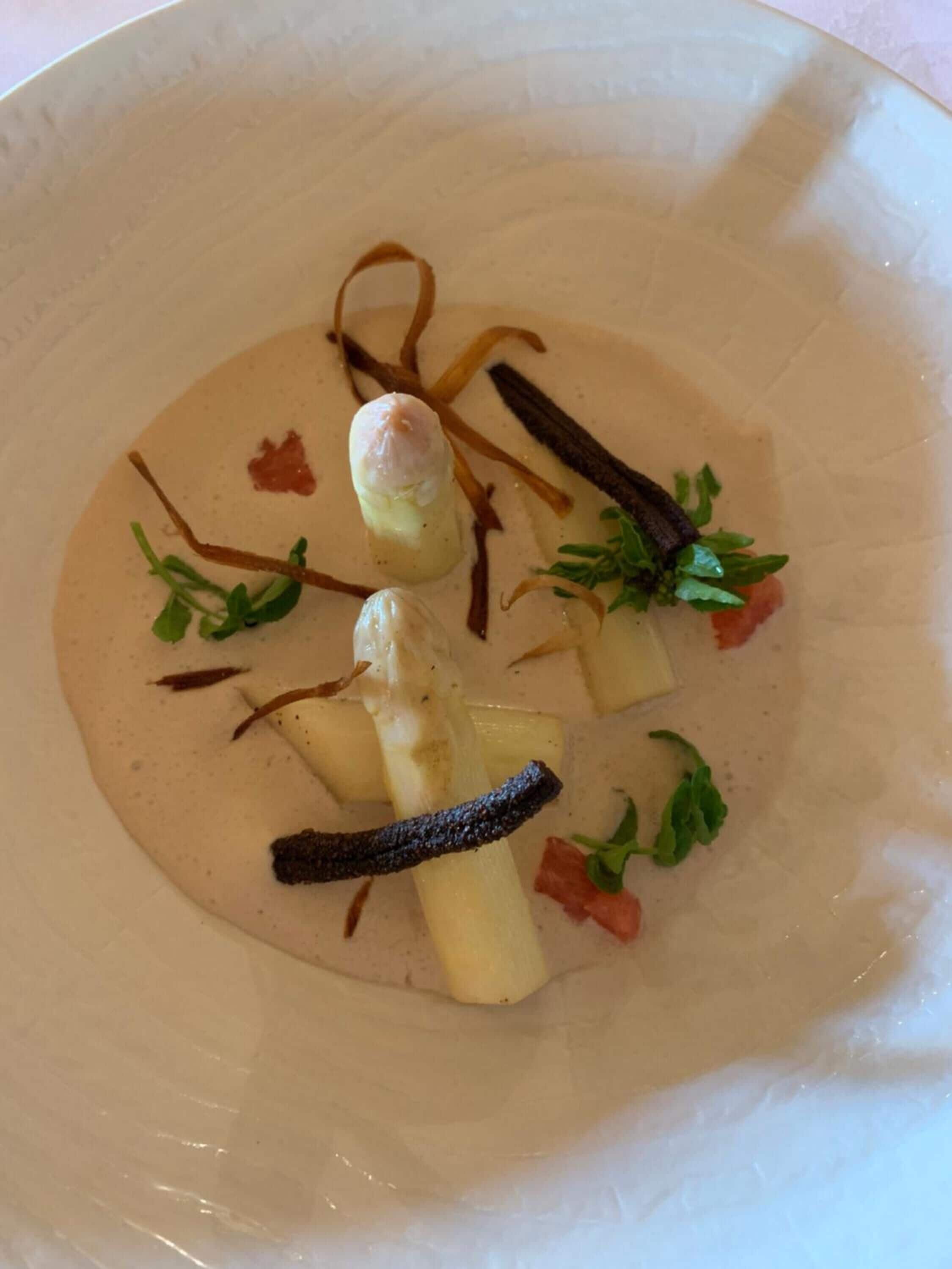 Une assiette blanche contenant une soupe crémeuse, garnie d’herbes et d’un morceau de carotte.
