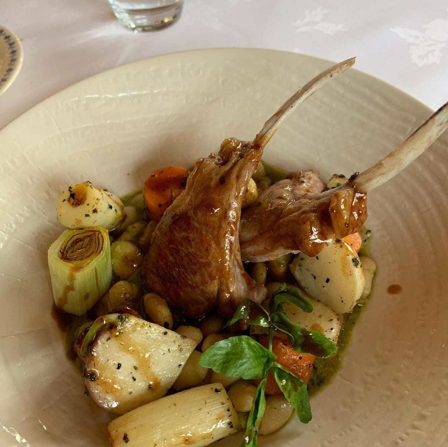 Une assiette de nourriture comprenant des côtelettes d’agneau, des pommes de terre, des carottes et des légumes verts.