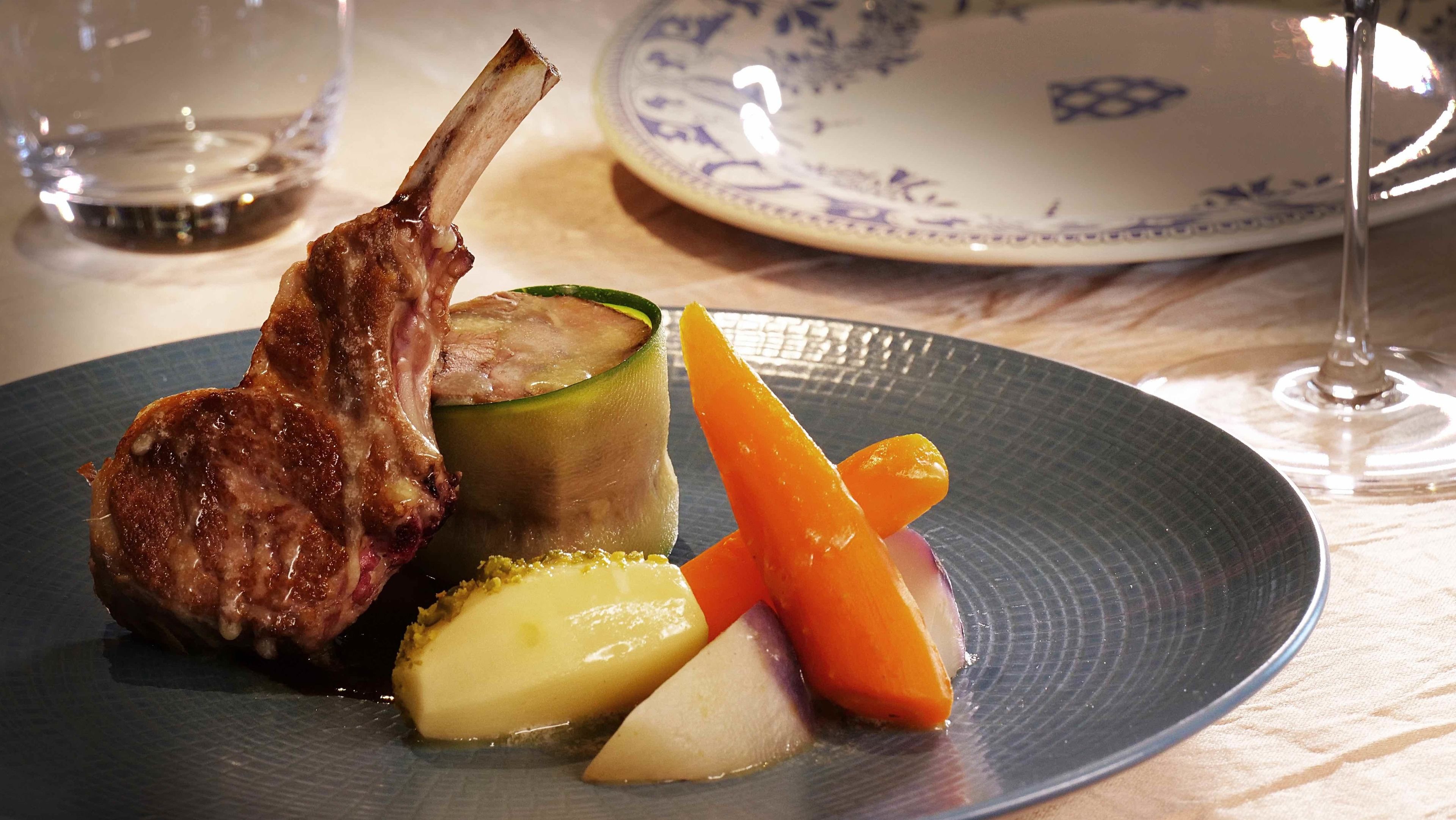 A plate with a lamb chop, zucchini, and carrots on a textured plate.