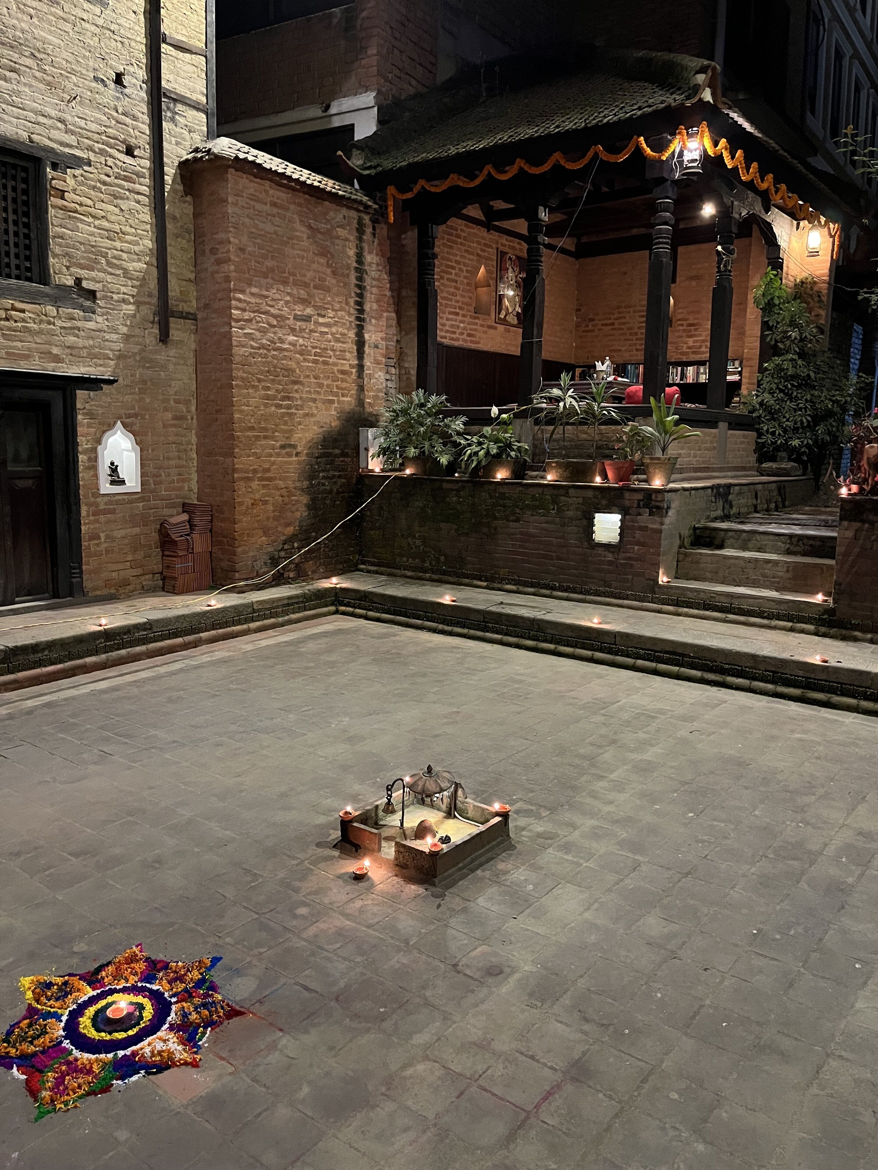 A courtyard with a small fountain, potted plants, and a traditional structure with a tiled roof.