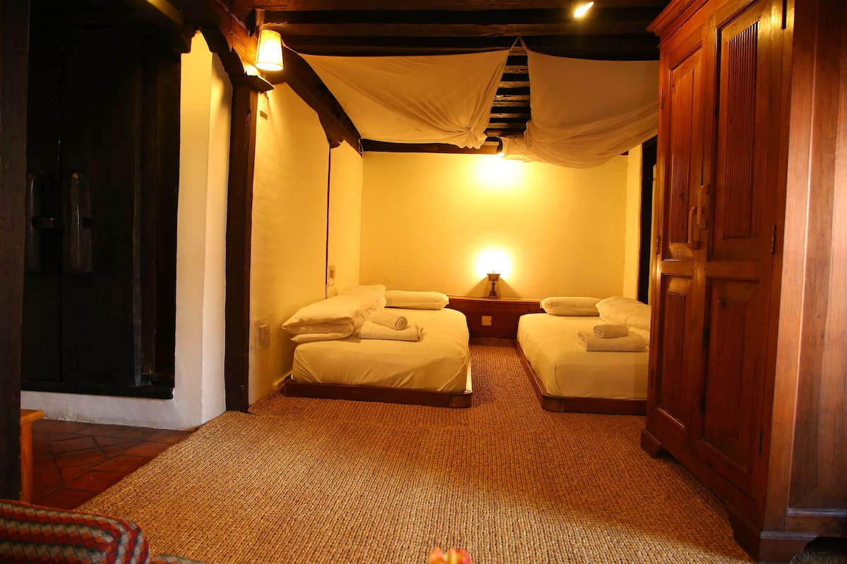 A room with two beds, a wooden wardrobe, and a carpeted floor.