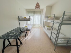 A dormitory room with bunk beds, a desk, and a hanging light fixture.