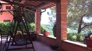 A covered patio with a swing set, potted plants, and a view of a building and trees. - Country Resort Al Poggio dei Papi (Citta della Pieve)