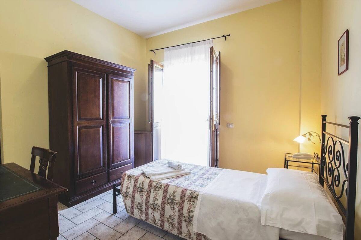 Un dormitorio con cama, armario, escritorio y ventana con cortinas.