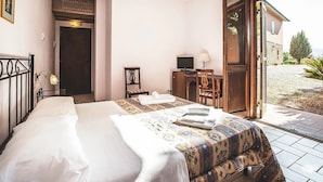 A bedroom with a bed, a desk with a computer, a chair, a small table, and a door leading to a balcony with a view of the outside. - Country Resort Al Poggio dei Papi (Citta della Pieve)