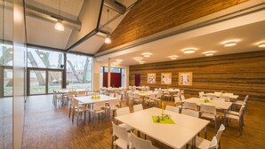 A spacious conference room with multiple tables and chairs, large windows, and wooden paneling on the walls. - Kloster Volkenroda (Körner)