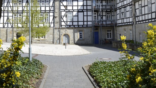A courtyard with a traditional half-timbered building, a paved walkway, and a blue door. - Kloster Volkenroda (Körner)