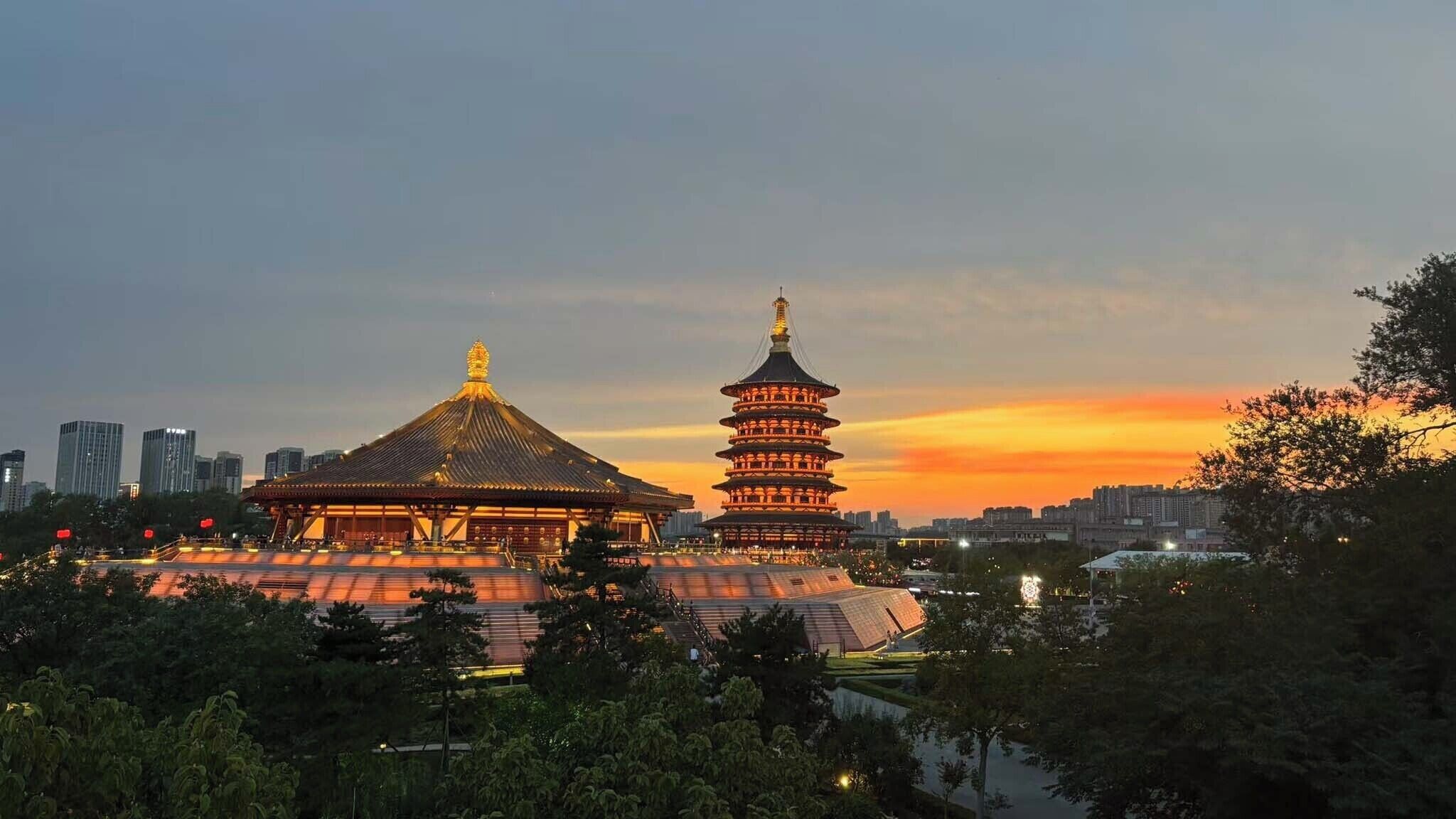 A traditional pagoda-style building with a tiered roof and a pagoda with multiple eaves, surrounded by trees and modern buildings in the background.