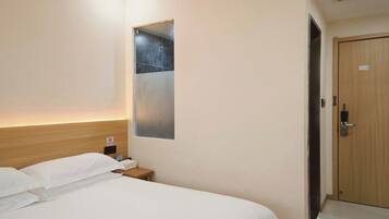 A hotel room with a bed, a nightstand, a mirror, and a door.