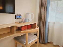 Habitación de hotel con escritorio de madera, televisor, cafetera y silla con cojín.