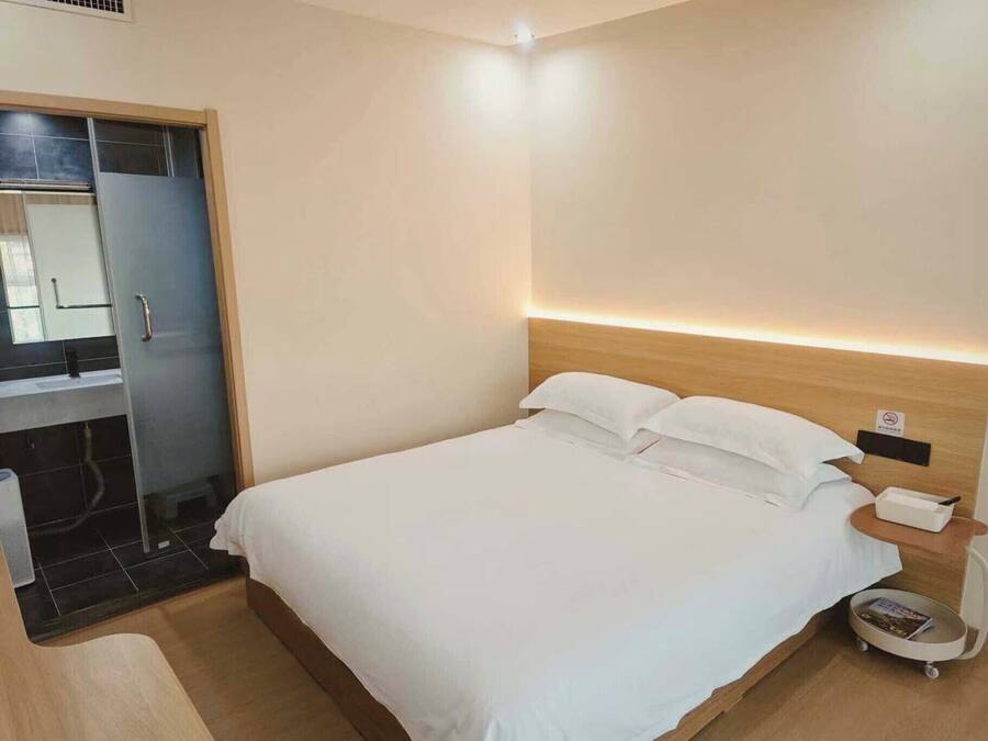 Una habitación de hotel con una cama, una mesita de noche, un carrito pequeño y un baño con ducha e inodoro.