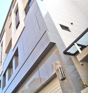 A modern building facade with a geometric design, large windows, and a visible air conditioning unit.