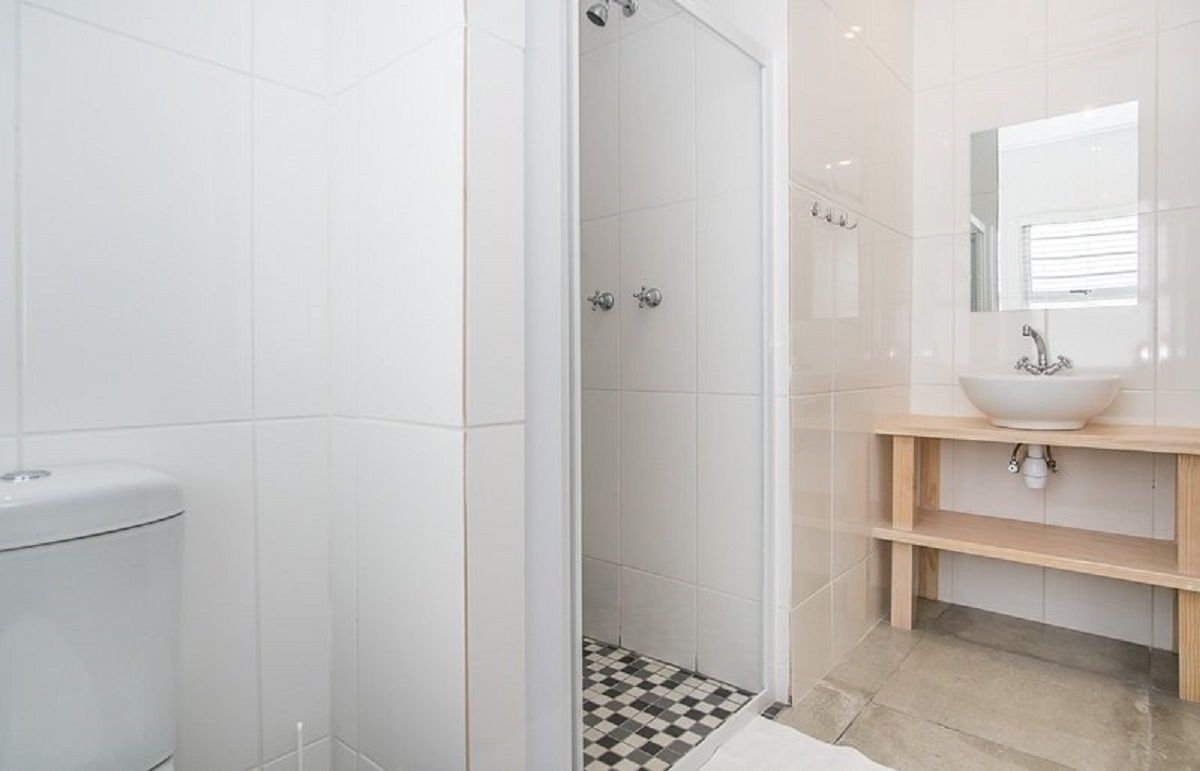 Een moderne badkamer met een douchecabine van glas, een wit wastafelmeubel met houten details en een vloer van zwart-wit ruitjes tegels.