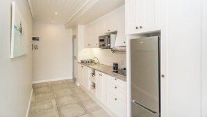 Una cocina compacta con armarios blancos, un refrigerador de acero inoxidable y un microondas.
