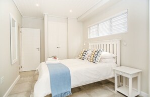 A bedroom with a bed, bedside table, and a window with blinds.