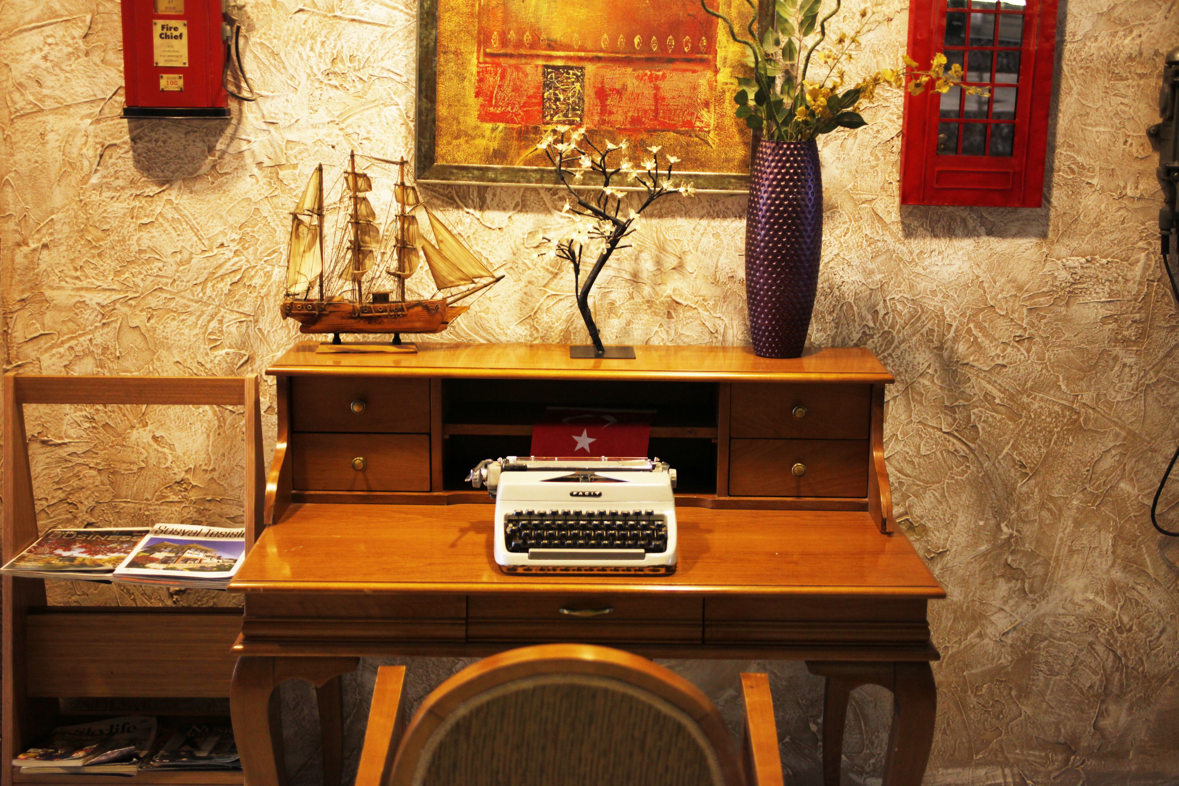 A wooden desk with a typewriter, a ship model, and a vase with flowers.