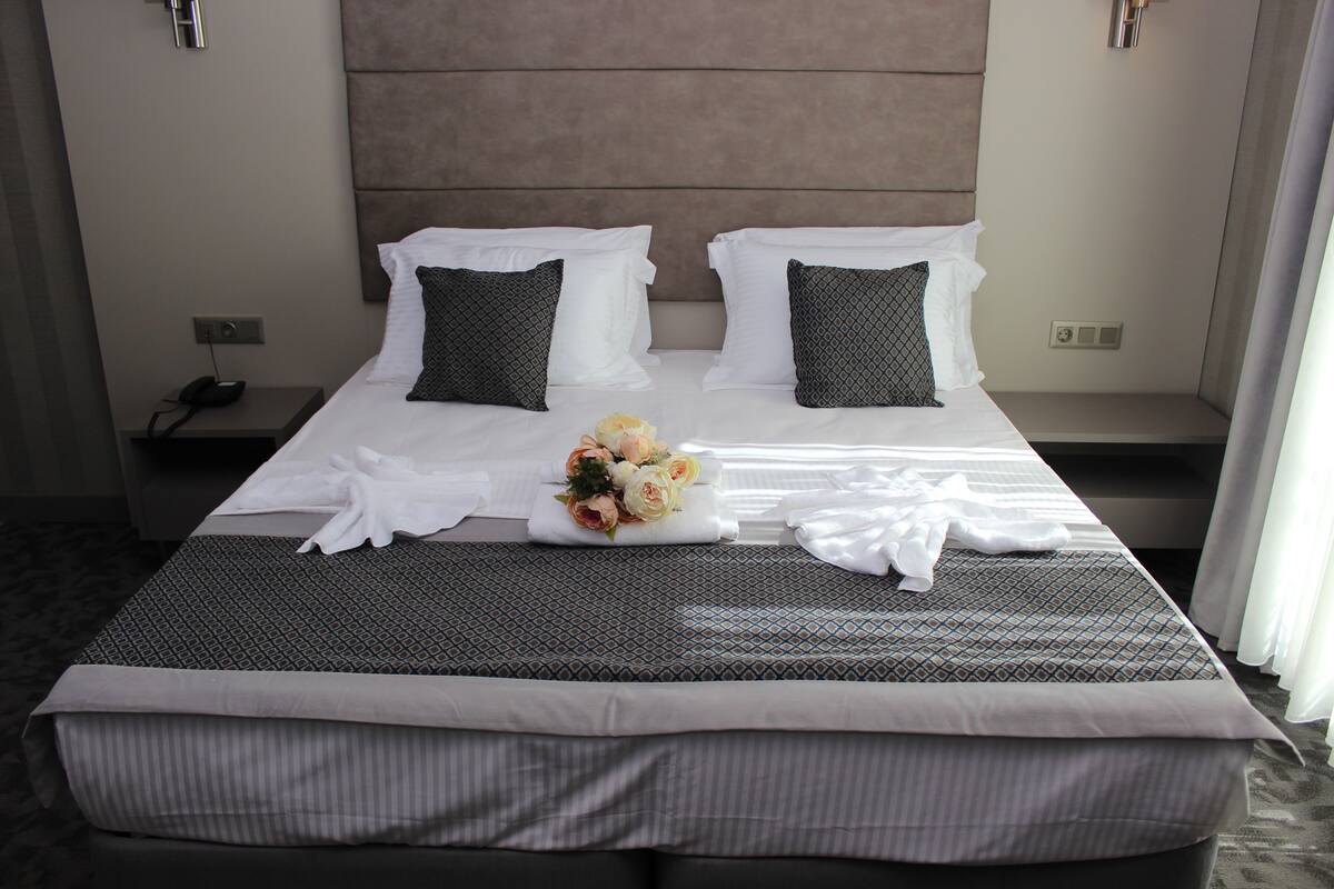 Una cama de hotel impecable con una colcha estampada, dos almohadas y un ramo de flores.
