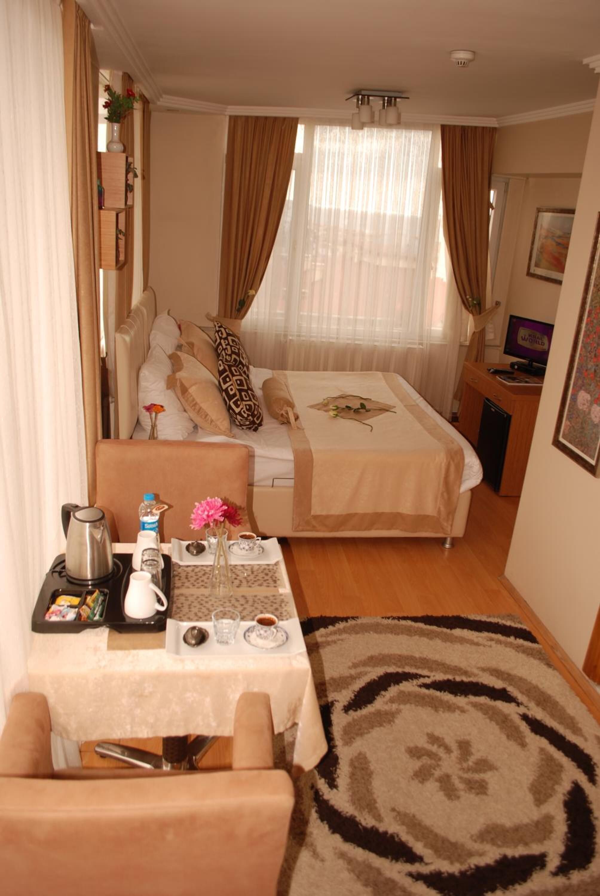 Ein Hotelzimmer mit Bett, Schreibtisch mit Computer, Kaffeemaschine und Tisch mit Blumenvase.