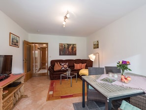 A living room with a sofa, coffee table, TV, and a dining area with a table and chairs.