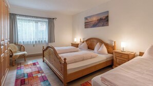 A bedroom with two wooden beds, a chair, a nightstand, and a window with curtains. - Ferienwohnung Nr. 4 für 2 - 4 Personen 55 qm (Kiefersfelden)