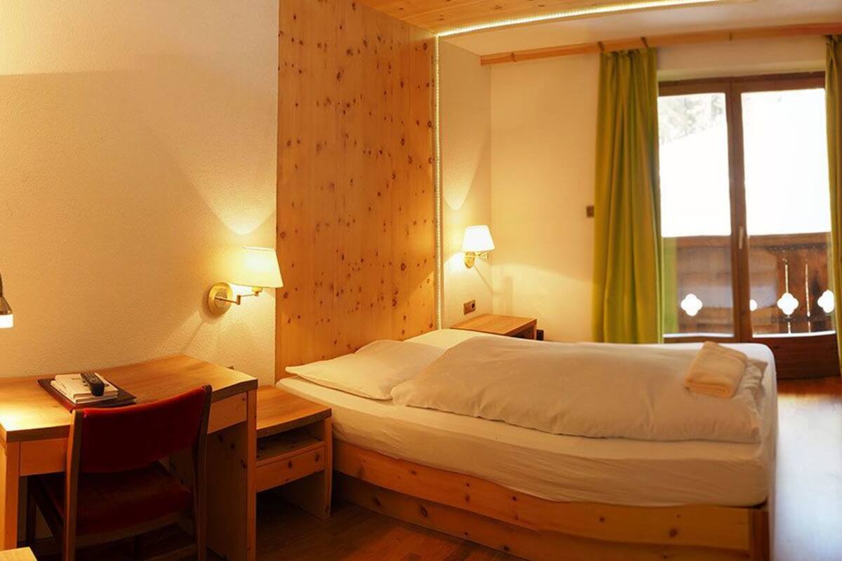 Una habitación acogedora con una cama de madera, un escritorio con silla y dos lámparas fijadas a la pared.