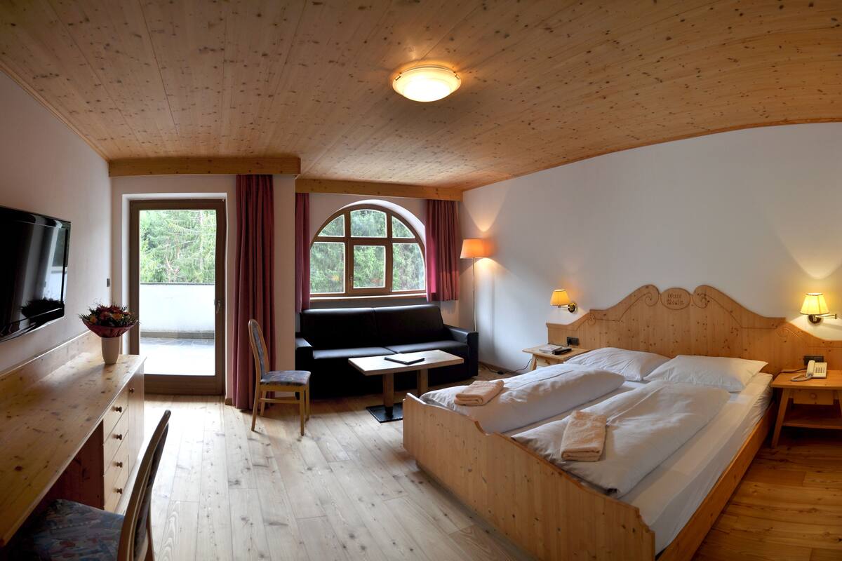 Una habitación de madera con una cama, un sofá, un televisor y una ventana con cortinas.