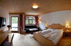 A wooden room with a bed, a sofa, a TV, and a window with curtains. - Berghotel Pine (Tires)