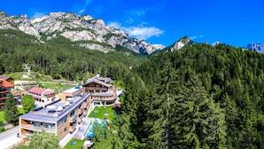 A mountain lodge with multiple buildings, a pool, and a forested backdrop. - Berghotel Pine (Tires)