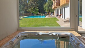 A hot tub with a view of a backyard swimming pool and a wooden deck. - Berghotel Pine (Tires)