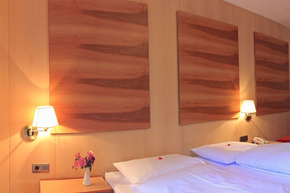 Habitación de hotel con cama, lámparas de noche, escritorio con silla, televisor y obras de arte en las paredes.