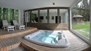 A hot tub on a wooden deck with two lounge chairs, a stone wall, and a view of a garden. - Berghotel Pine (Tires)