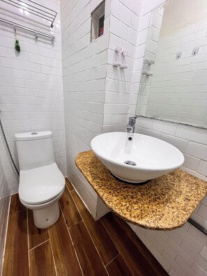 Un baño con inodoro blanco, lavamanos de encimera de granito y un espejo arriba.