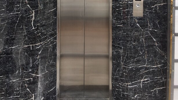 An elevator with a metallic finish, set against a black marble wall with white veins. - An Nam Corner Dreamer (Ho Chi Minh City)
