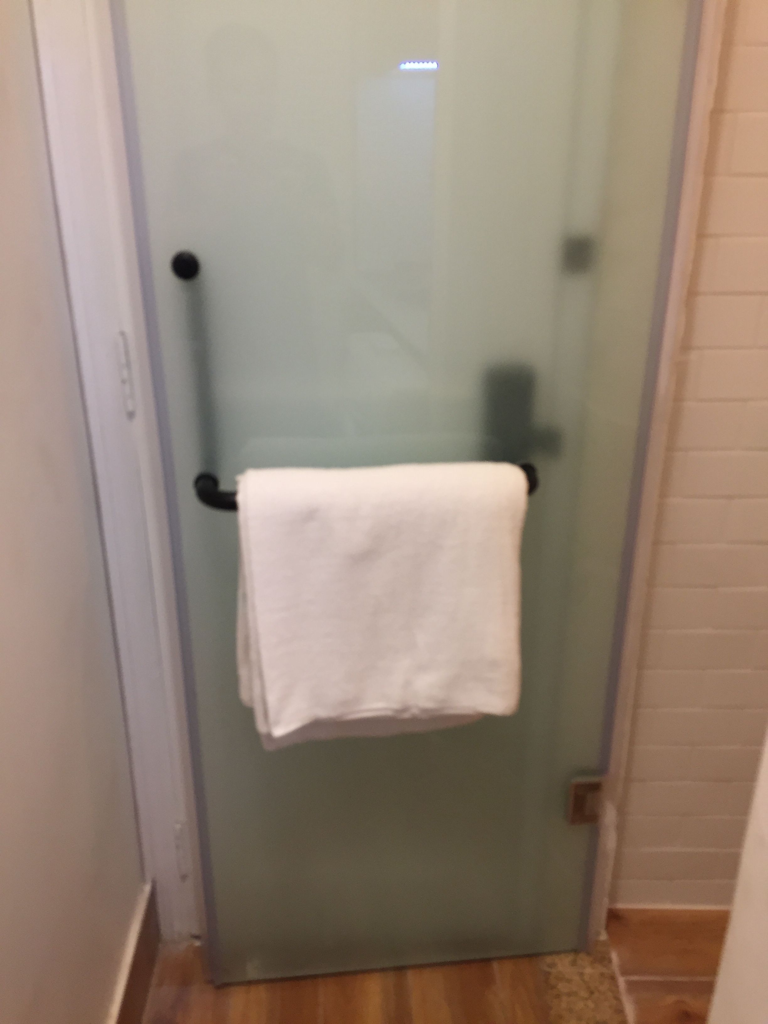A glass door with a towel hanging on a black towel rack.