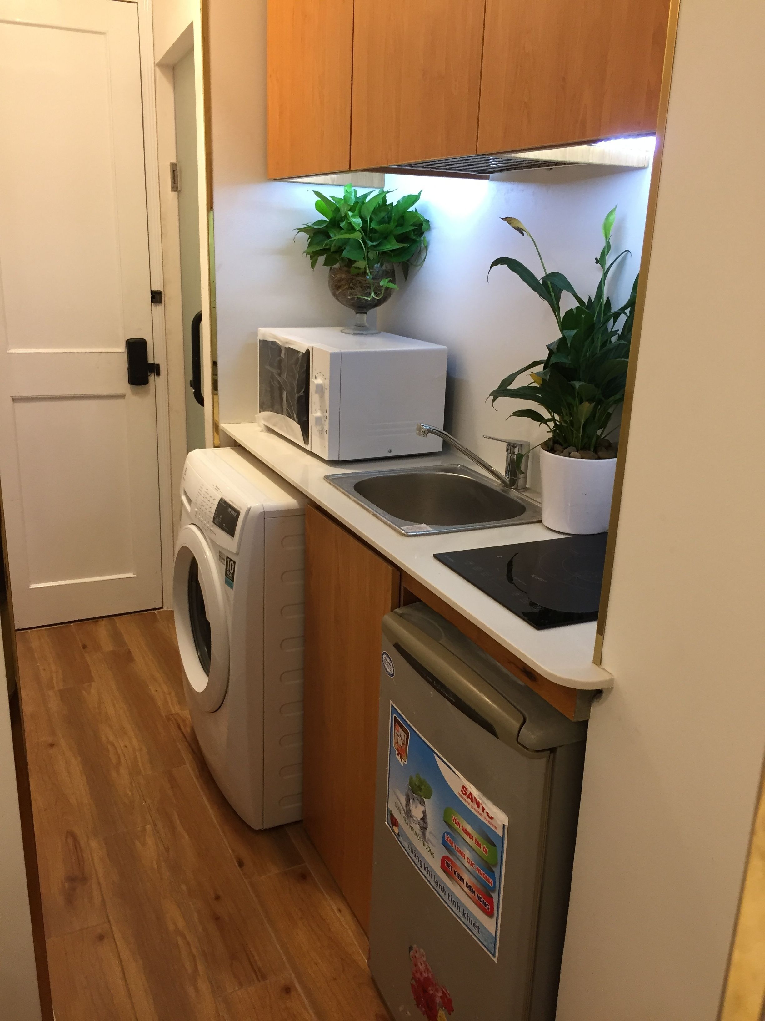 Cozinha compacta com máquina de lavar, micro-ondas, pia e um pequeno frigorífico.